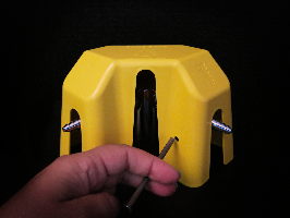 Image of a counter-mounted Burner Brake covering a gas jet fixture; this Burner Brake is equipped with a removable fastener that is being inserted.